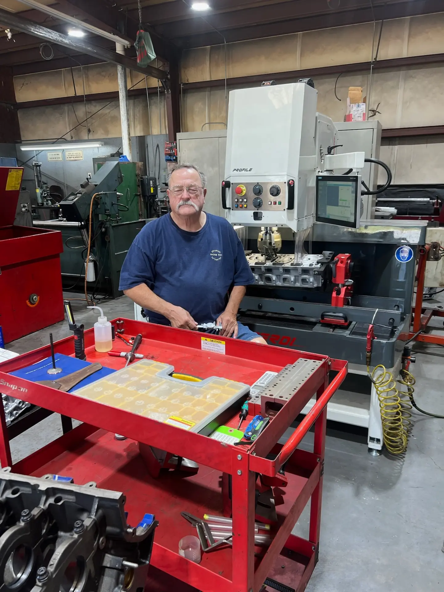 John Potts at the workbench inside Champion Automotive Machine Shop, with the Profile valve seat and guide machine behind him